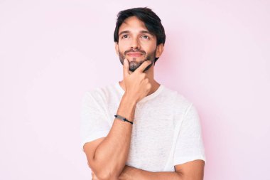 Yakışıklı, beyaz tişört giyen, yakışıklı, ciddi yüzlü, eli çenesinde soru soran, kafa karıştırıcı bir fikir. 