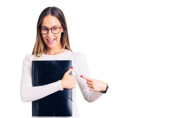 Güzel esmer, genç bir kadın iş dosyasını tutuyor. Gülümsüyor, mutlu bir şekilde eli ve parmağı işaret ediyor. 