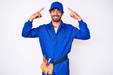 Kıvırcık saçlı ve ayı gibi giyinen yakışıklı genç adam gülümseyerek iki eliyle başını işaret ediyor, harika fikir ya da düşünce, iyi hafıza 