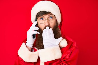 Uzun sakallı, yakışıklı, Noel Baba kostümü giyen, ağzı eliyle kapatan ve hata yapmaktan korkan genç, kızıl saçlı adam. şaşırmış ifade 