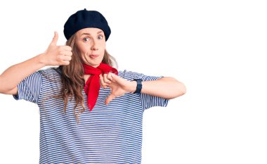 Fransız beresi takan, çizgili tişört giyen, baş parmak hareketi yapan genç, güzel sarışın bir kadın. Anlaşmazlık ve uzlaşma ifadesi. çılgın çatışma 