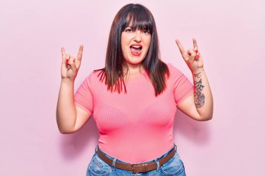 Genç ve cüsseli bir kadın gündelik kıyafetler giyip çılgın bir ifadeyle bağırıyor ve elleri havada rock sembolü yapıyor. Müzik yıldızı. ağır kavram. 