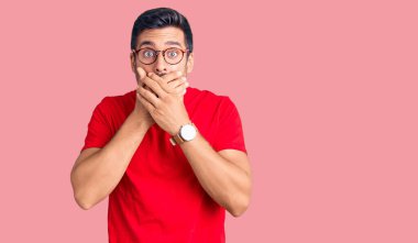 Günlük kıyafet ve gözlük takan genç İspanyol adam yanlışlıkla elleri ile ağzını kapatırken şok oldu. gizli kavram. 