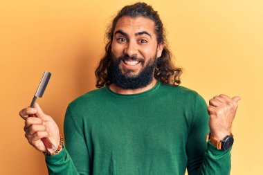 Genç Arap adam berber jileti tutuyor. Parmağını yana doğru uzatıyor. Gülümsüyor, ağzı açık. 