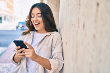 Genç İspanyol kadın şehirde akıllı telefon kullanarak mutlu bir şekilde gülümsüyor..