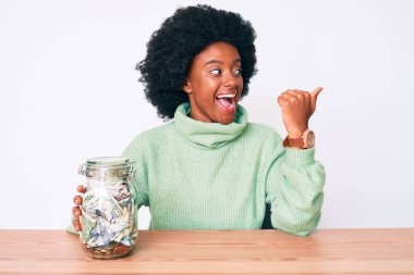 Afro-Amerikalı genç bir kadın elinde kavanozla başparmağını kaldırmış, ağzı açık bir şekilde gülümsüyor. 