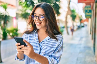Genç İspanyol iş kadını şehirde akıllı telefon kullanarak mutlu gülümsüyor..