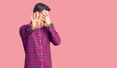 Ayı gömleği giyen yakışıklı genç adam elleriyle gözlerini kapatıyor ve üzgün ve korku ifadeleriyle jest yapıyor. utangaç ve olumsuz kavram. 