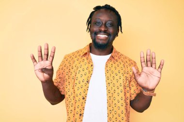 Saçları örgülü genç Afro-Amerikan bir adam 9 numarayı gösterip gösterirken kendinden emin ve mutlu bir şekilde gülümsüyor.. 