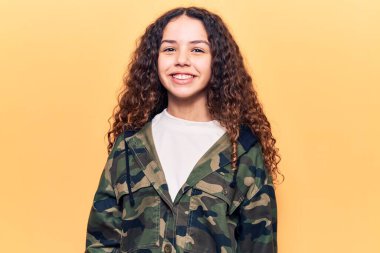 Kıvırcık saçlı, kamuflaj ceket giyen güzel bir kız. Pozitif ve mutlu görünüyor. Kendine güvenen bir gülümsemeyle dişlerini gösteriyor. 
