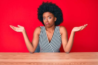 Genç Afrikalı Amerikalı kadın gündelik giysiler giyiyor, habersiz ve kolları açık, hiçbir fikrim yok ve şüpheli bir yüzüm var.. 