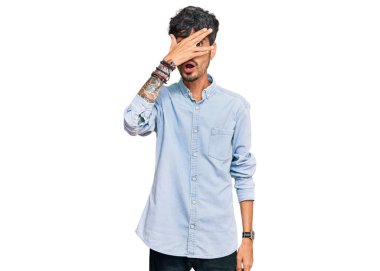 Gündelik kıyafetler giyen genç İspanyol adam şok içinde yüzünü ve gözlerini kapayarak utanmış ifadesiyle parmaklarından bakıyor.. 