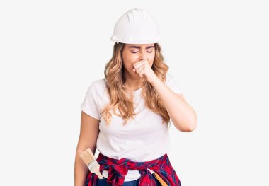 Güvenlik kaskı takan beyaz bir kadın kendini iyi hissetmiyor ve soğuk algınlığı veya bronşitin belirtisi olarak öksürüyor. sağlık hizmeti kavramı. 