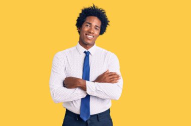 Afro saçlı, iş kıyafetleri giyen, kollarını kavuşturup kameraya gülümseyen yakışıklı Afro-Amerikan bir adam. pozitif kişi. 
