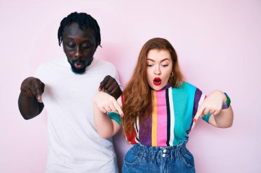 Irklar arası giysiler giyen, parmaklarını göstererek reklamını yapan, şaşırmış yüzlü ve ağzı açık bir çift. 