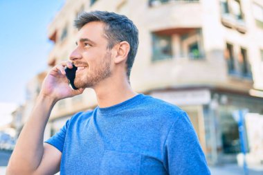 Genç beyaz adam gülümsüyor. Şehirdeki akıllı telefondan konuşuyor..