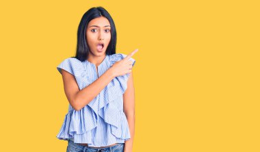 Gündelik kıyafetler giyen genç ve güzel bir Latin kız parmaklarını yana doğru göstererek şaşırdı, ağzı açık hayret içinde kaldı.. 