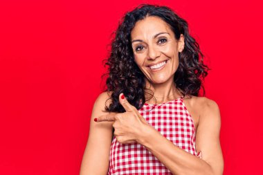 Orta yaşlı, kolsuz tişört giyen güzel bir kadın. Gülümsüyor, eli ve parmağı yana doğru uzanıyor. 