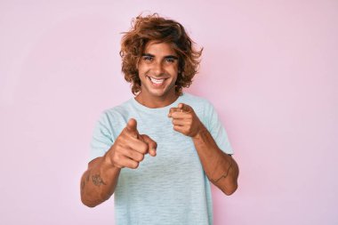 Günlük kıyafetler giyen genç İspanyol adam mutlu ve komik yüzüyle kamerayı işaret ediyor. iyi enerji ve titreşimler. 