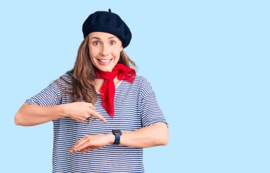 Fransız beresi ve çizgili tişört giyen genç, güzel sarışın kadın. Saati, sabırsızlığı ve gecikmeyi işaret ediyor. 