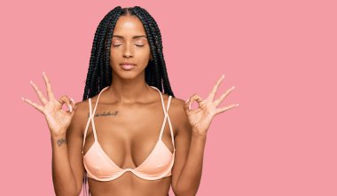 Güzel İspanyol kadın bikini giyip rahatlıyor ve gözleri kapalı gülümsüyor parmaklarıyla meditasyon hareketi yapıyor. yoga konsepti. 