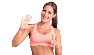 Genç ve güzel İspanyol kadın spor giysisi giyiyor. Altıncı parmaklarıyla işaret ediyor ve gülümsüyor. Kendinden emin ve mutlu.. 