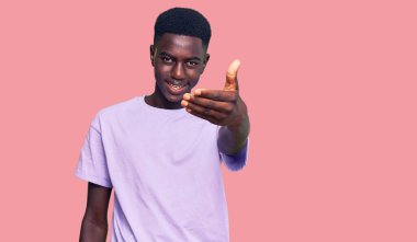 Genç Afro-Amerikan adam günlük kıyafetler giyip gülümseyerek dostça el sıkışarak selamlama ve hoş geldin diyor. başarılı iş. 