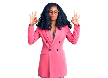 Güzel Afro-Amerikalı kadın iş ceketi ve gözlük takıyor rahatlıyor ve gözleri kapalı gülümsüyor parmaklarıyla meditasyon hareketi yapıyor. yoga konsepti. 