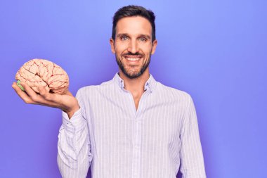 Genç ve yakışıklı bir adam, beyni mor arka planda tutmak için özenli bir hatıra istiyor. Olumlu ve mutlu görünüyor. Kendine güvenen bir gülümsemeyle dişlerini gösteriyor.