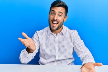 İş kıyafetleri giymiş yakışıklı İspanyol adam masaya oturmuş gülümsüyor, yardım eli uzatıyor ve kabul ediyor.. 