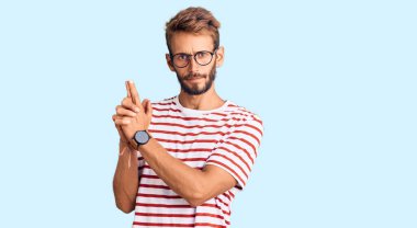 Sakallı, sıradan kıyafetler ve gözlük takan, el hareketleriyle sembolik silah tutan, cinayet silahlarıyla oynayan, sinirli yüzlü, yakışıklı sarışın bir adam. 