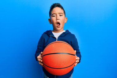 Küçük İspanyol çocuk basketbol topunu suratında tutuyor, şüpheci ve alaycı görünüyor, ağzı açık kalınca şaşırıyor. 