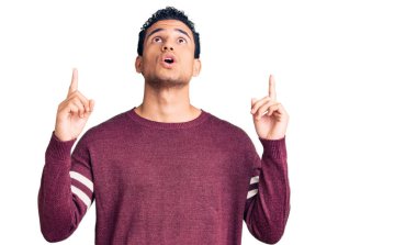 İspanyol görünümlü, sıradan kıyafetler giyen genç adam şaşırmış ve şaşırmış bir şekilde yukarı baktı ve parmaklarıyla işaret ederek kollarını kaldırdı.. 