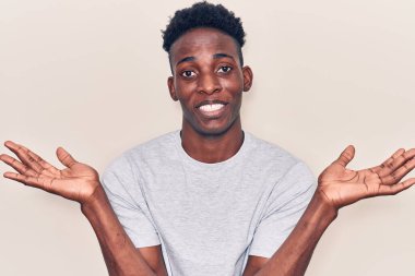 Sıradan kıyafetler giyen, kafası karışmış, elleri ve kolları havada genç Afro-Amerikalı bir adam. şüphe kavramı. 