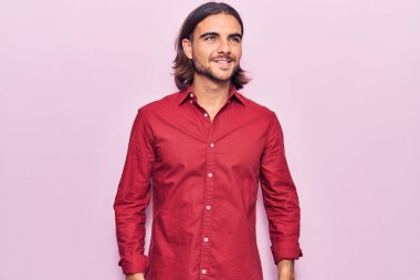 İş kıyafetleri giymiş, yüzünde gülümsemeyle yan yana bakan yakışıklı bir genç. Doğal bir ifade. Kendinden emin gülen. 