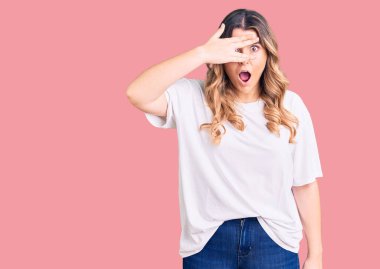 Gündelik giysiler giymiş genç beyaz kadın şok içinde yüzünü ve gözlerini kapayarak utanmış ifadesiyle parmaklarından bakıyor.. 