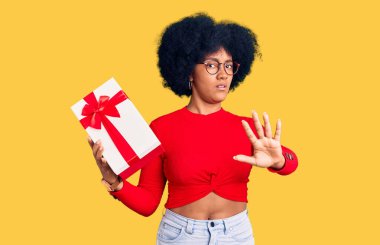 Genç Afrikalı Amerikalı kız elinde hediyeyle avuç içi hareketlerini durduruyor, kızgın ve hayal kırıklığı dolu bir ifade takınıyor. 