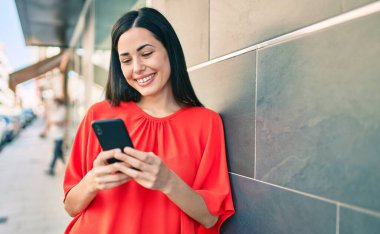 Genç Latin kız şehirde akıllı telefon kullanarak mutlu bir şekilde gülümsüyor..