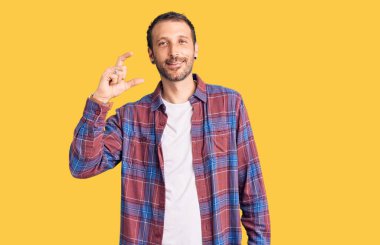 Gündelik kıyafetler giyen, gülümseyen, kendine güvenen, el hareketleriyle küçük boy işareti yapan, parmaklarıyla işaret eden ve kameraya bakan genç yakışıklı bir adam. ölçüm kavramı. 