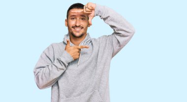 Dövmeleri olan, sıradan bir kazak giyen, gülümseyen, elleri ve parmakları mutlu yüzlü yakışıklı bir adam. yaratıcılık ve fotoğrafçılık kavramı. 