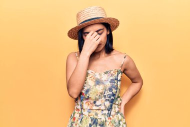 Yazlık şapka takan, burnu ve gözleri ovuşturmaktan yorgun, yorgun ve başı ağrıyan genç, güzel Latin bir kadın. Stres ve hüsran kavramı. 