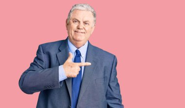 Yaşlı, gri saçlı, iş ceketi giyen, neşeli, yüzünde bir gülümseme olan, mutlu ve doğal bir ifadeyle elini ve parmağını yana gösteren bir adam. 