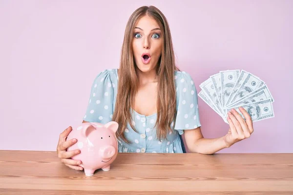 Jong Blond Meisje Met Dollars Spaarvarken Zitten Tafel Bang Geschokt — Stockfoto