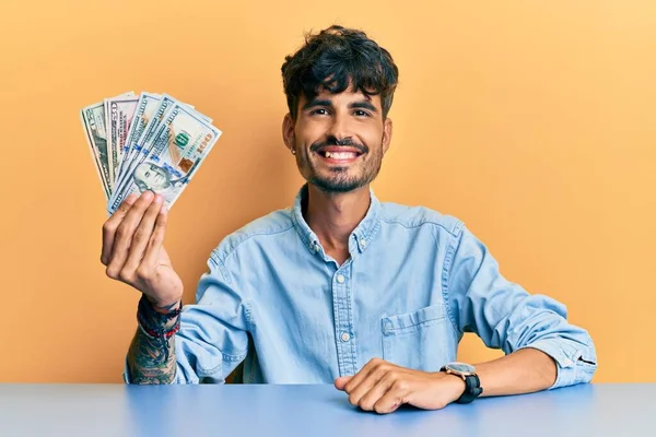 Joven Hombre Hispano Sosteniendo Dólares Sentado Mesa Luciendo Positivo Feliz — Foto de Stock