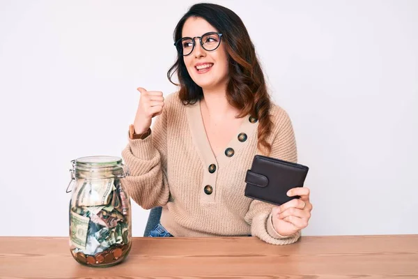 Joven Hermosa Morena Sosteniendo Frasco Con Ahorros Sosteniendo Cartera Apuntando — Foto de Stock