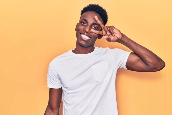 顔の上に指で平和のシンボルを行うカジュアルな服を着て若いアフリカ系アメリカ人の男 勝利を示す明るい笑顔 — ストック写真