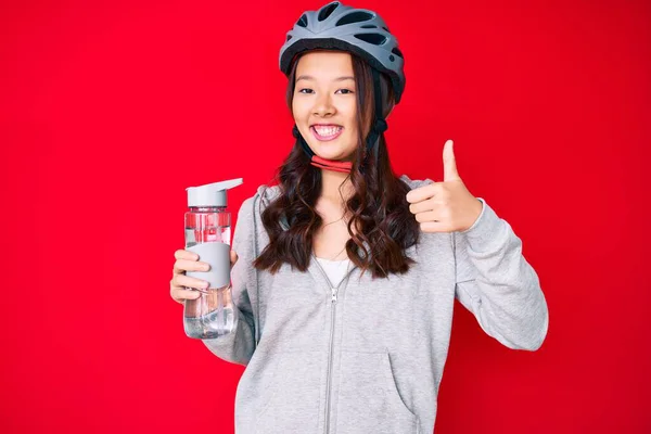 若い美しい中国の女の子は自転車のヘルメットを着て 水のボトルを保持笑顔幸せと正 親指アップ行う優れた承認サイン — ストック写真