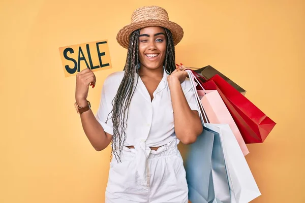 Junge Afrikanisch Amerikanische Frau Mit Zöpfen Einkaufstaschen Und Verkaufsbanner Zwinkernd — Stockfoto