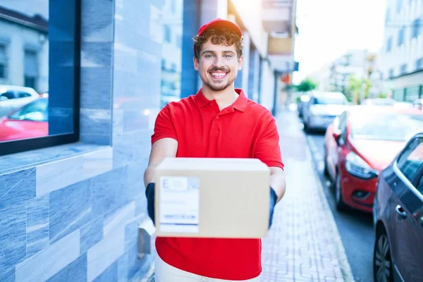 Young Caucasian Delivery Man Smiling Happy Holding Cardboard Package Walking — Stock Photo, Image