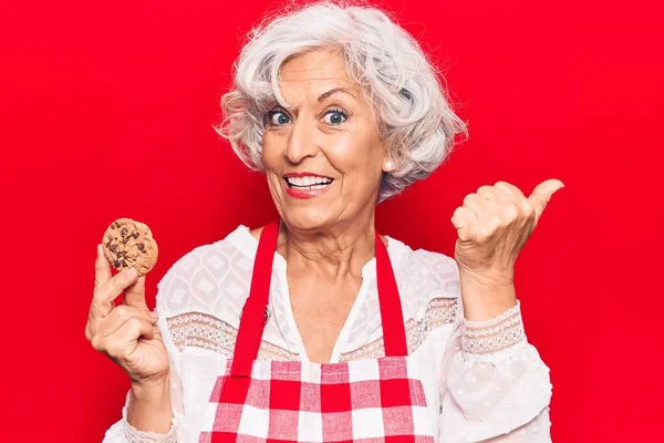 Senior Mujer Pelo Gris Con Delantal Sosteniendo Galleta Apuntando Pulgar — Foto de Stock